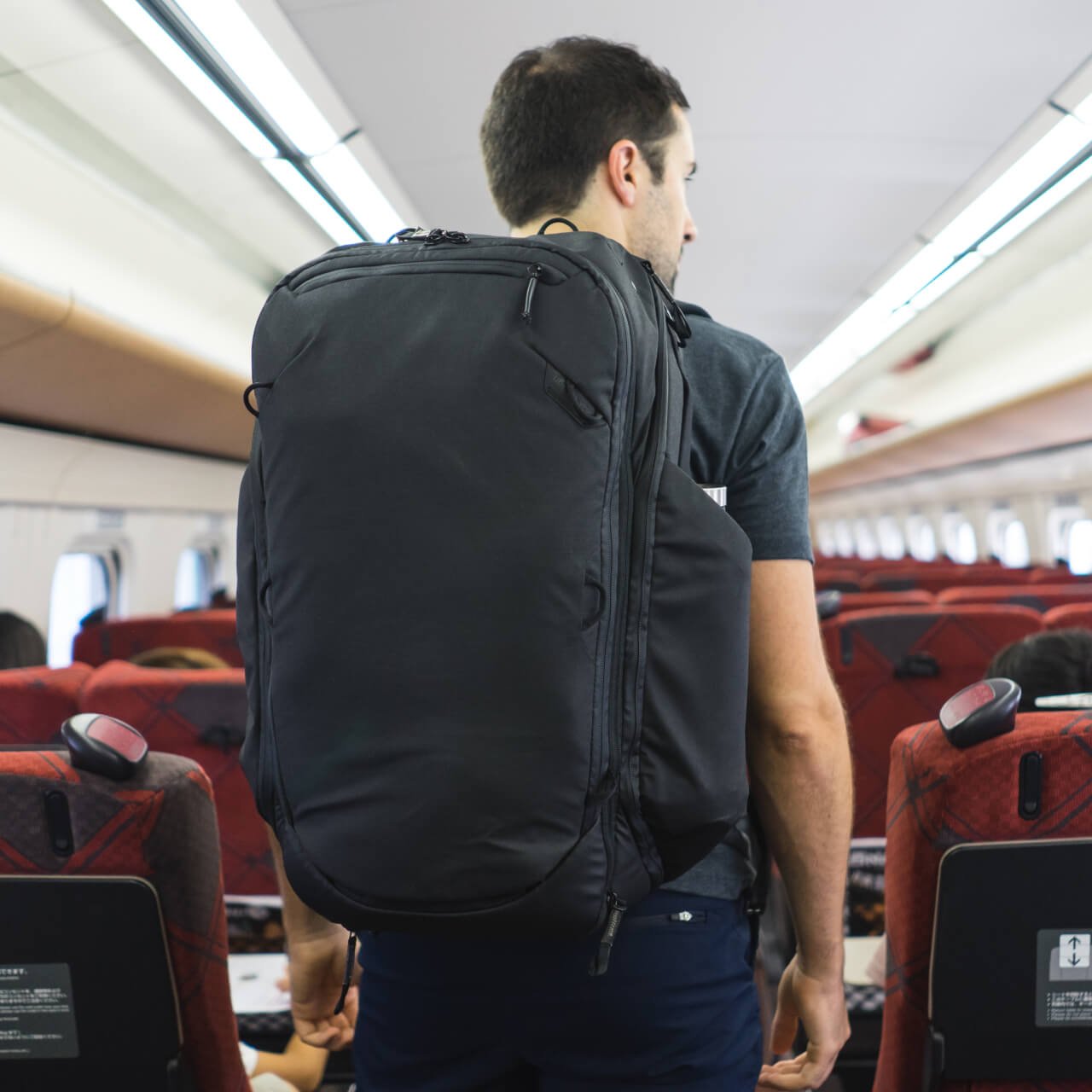 Peak Design Travel Backpack 45L being lifted into an aircraft overhead bin as carry-on