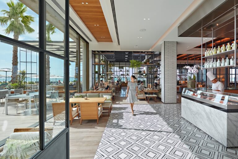 Interior of The Bay all-day brasserie at Mandarin Oriental Jumeira, Dubai, with floor-to-ceiling windows onto palms and the sea