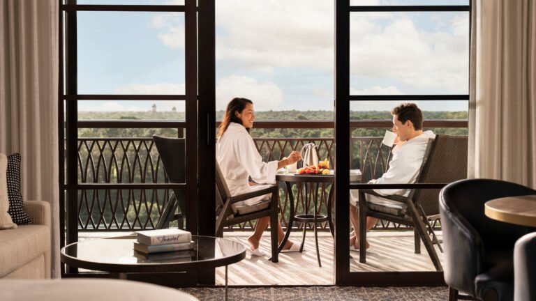 Couple in robes enjoying in-room breakfast on a private guest-room balcony overlooking woodland