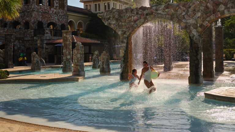Mother and child playing under a stone-arch waterfall fountain in the splash zone at Explorer Island water park