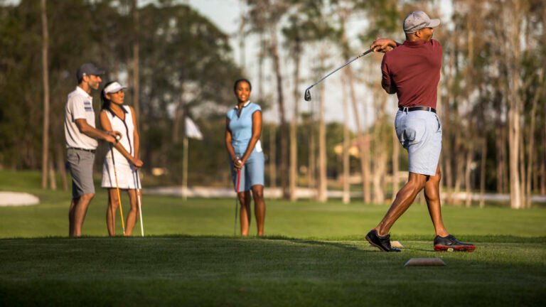 Foursome of golfers on the Tranquilo championship course, one mid-swing on the tee at golden hour
