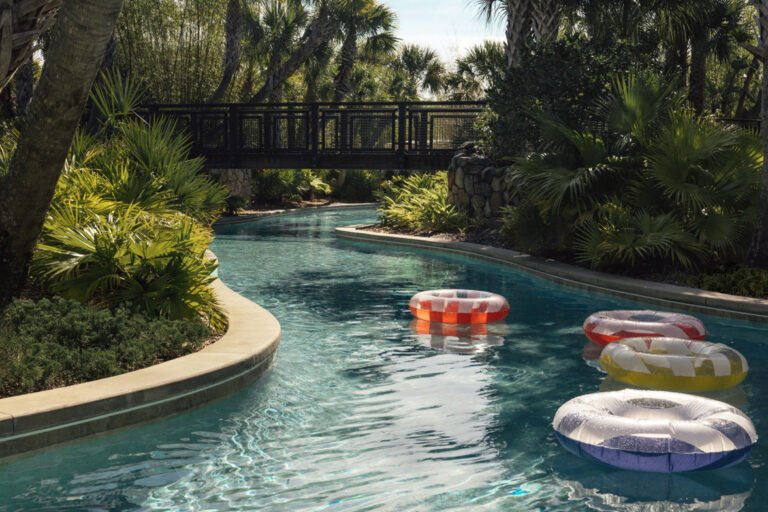 Lazy river with floating tubes winding under a footbridge through lush tropical planting