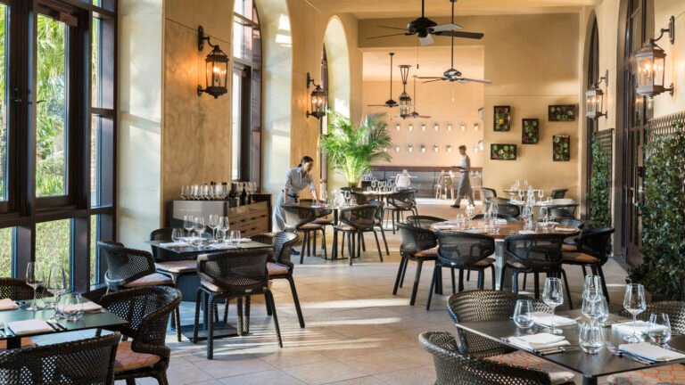 Elegant arched dining room with tall windows, lanterns and a wine display being set for service