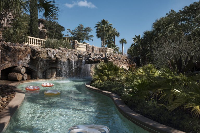 Colorful inner tubes drifting along the lazy river past a stone waterfall and palms at Explorer Island