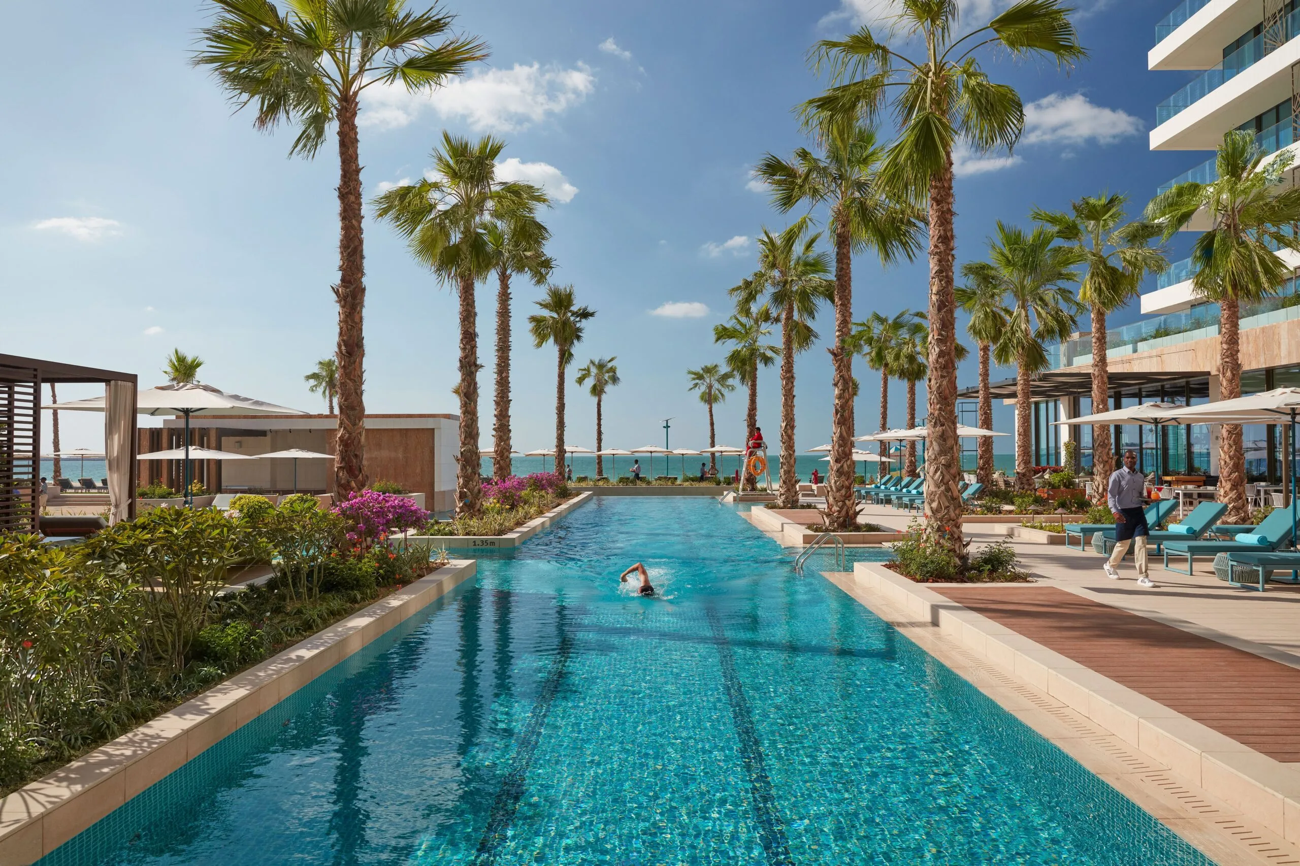 Outdoor pool lined with palm trees and cabanas at Mandarin Oriental Jumeira, Dubai, with the Arabian Gulf beyond