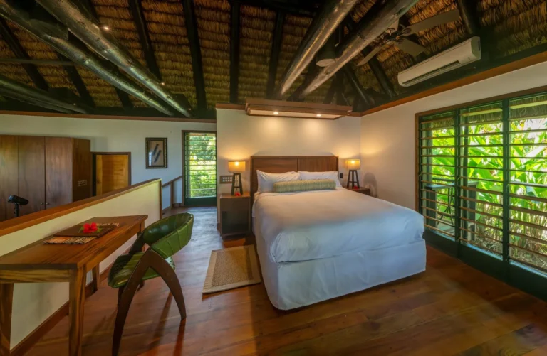 Bedroom of the Oceanfront Point Reef Bure at Jean-Michel Cousteau Resort Fiji, with an exposed timber ceiling and split-level layout