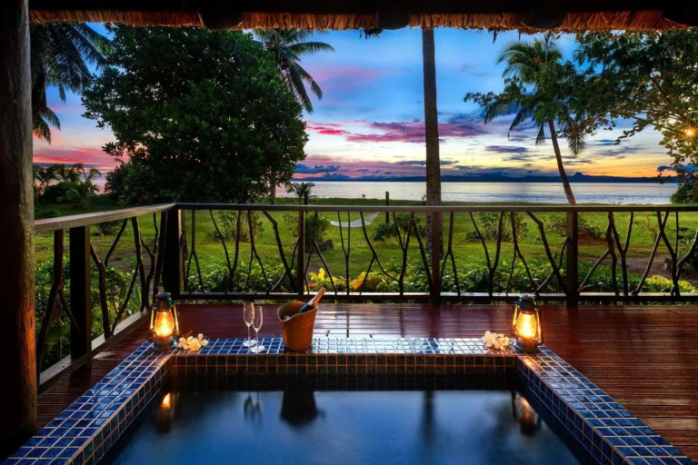Private outdoor spa tub on the deck of the Oceanfront Point Reef Spa Tub Bure at Jean-Michel Cousteau Resort Fiji, at sunset