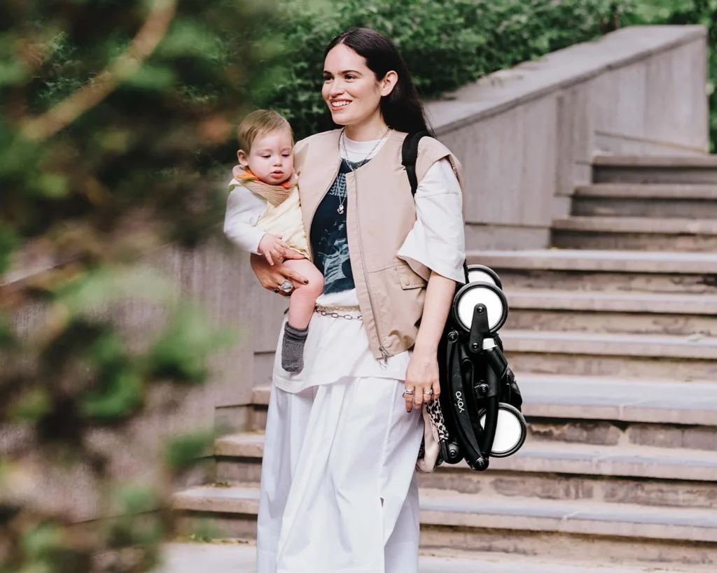 Parent carrying the folded Stokke YOYO3 over the shoulder while holding a baby