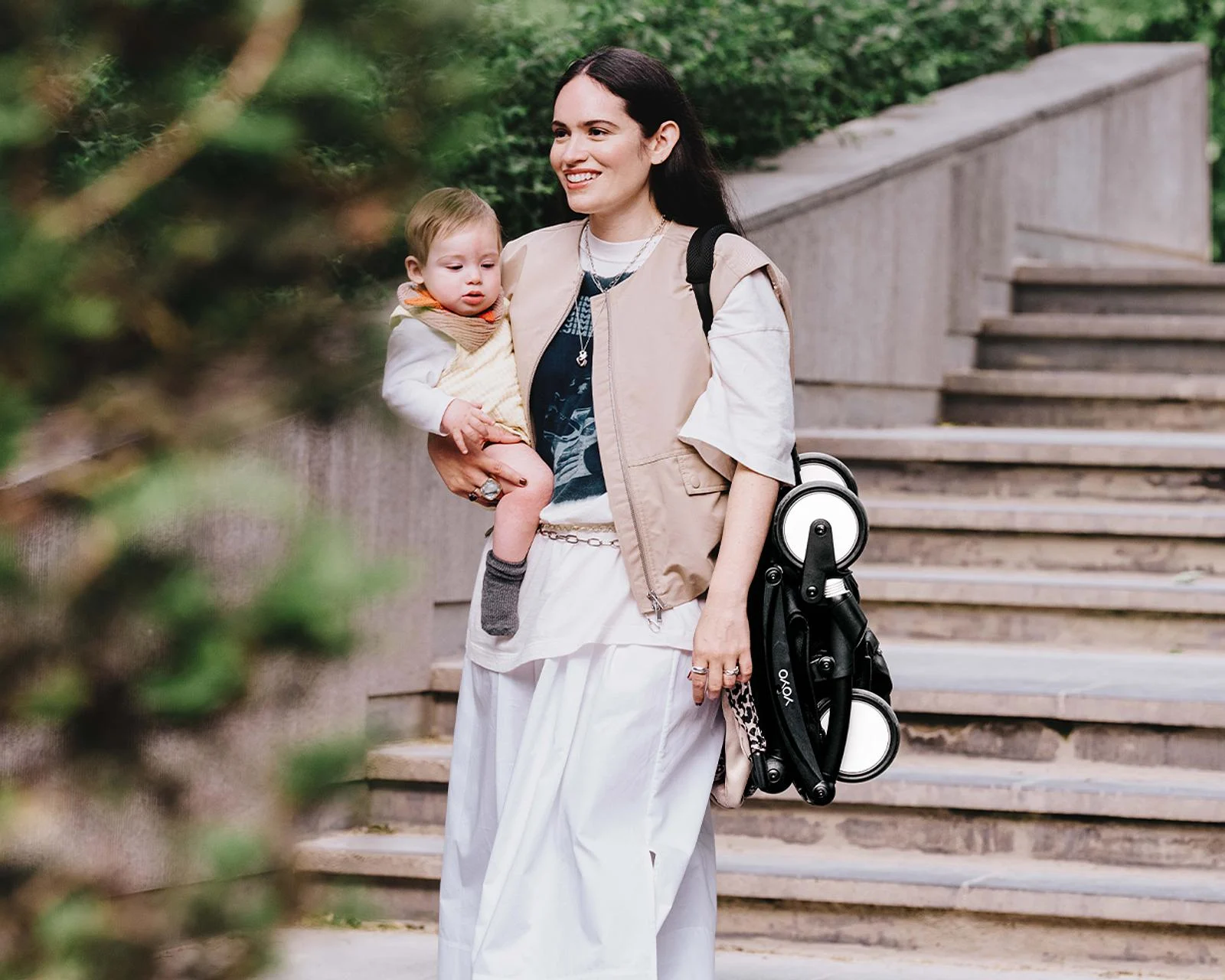 Parent carrying the folded Stokke YOYO3 over the shoulder while holding a baby