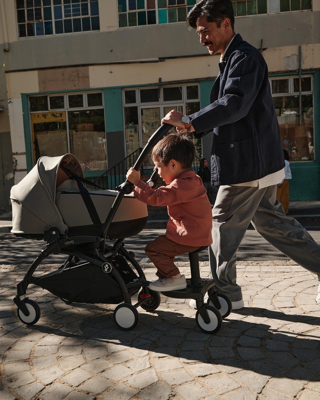 Father pushing the Stokke YOYO3 with an older child riding the sibling board