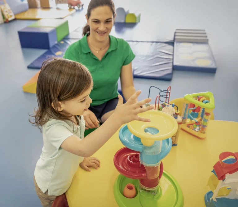 Kleinkind mit Betreuerin an einem Motorikspielzeug in der Crèche