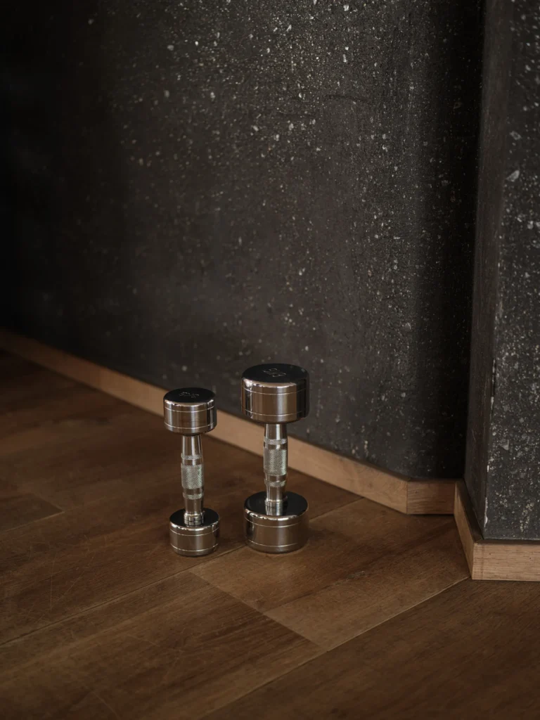 The bright, well-equipped fitness centre at Sonnwies with cardio machines facing floor-to-ceiling windows over the pine forest and a rack of free weights along one wall.