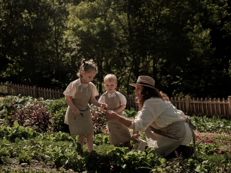 A group of children laugh and run together across a sun-dappled outdoor terrace at Family Hotel Sonnwies, watched by a smiling children's entertainer.