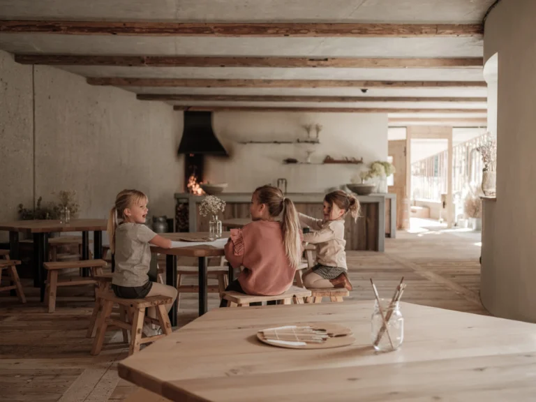 Children sit around a wide wooden workbench in the Sonnwies Manufaktur, each pressing dough or painting ceramic pieces under the guidance of a Ferdi's World team member.