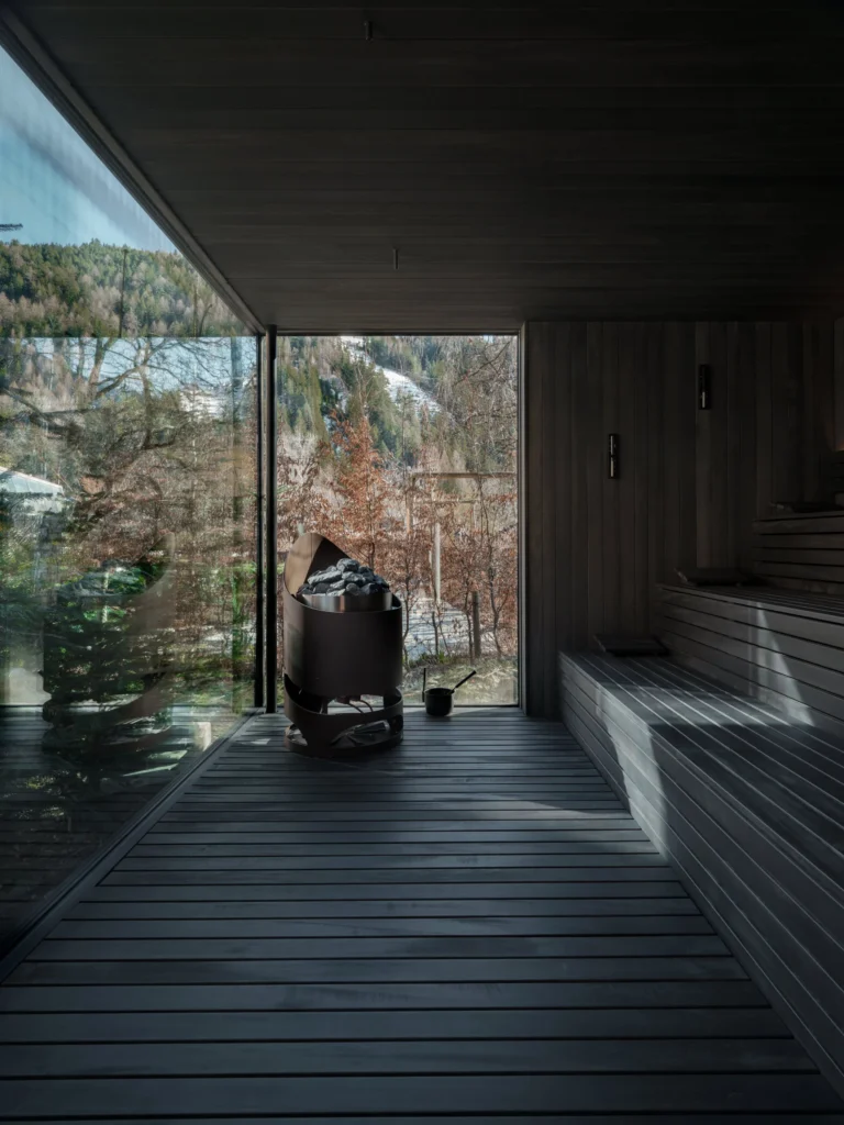 A couple share a large outdoor hot tub on a private timber deck at Sonnwies, steam rising around them as they gaze out at the snow-dusted Dolomite peaks.