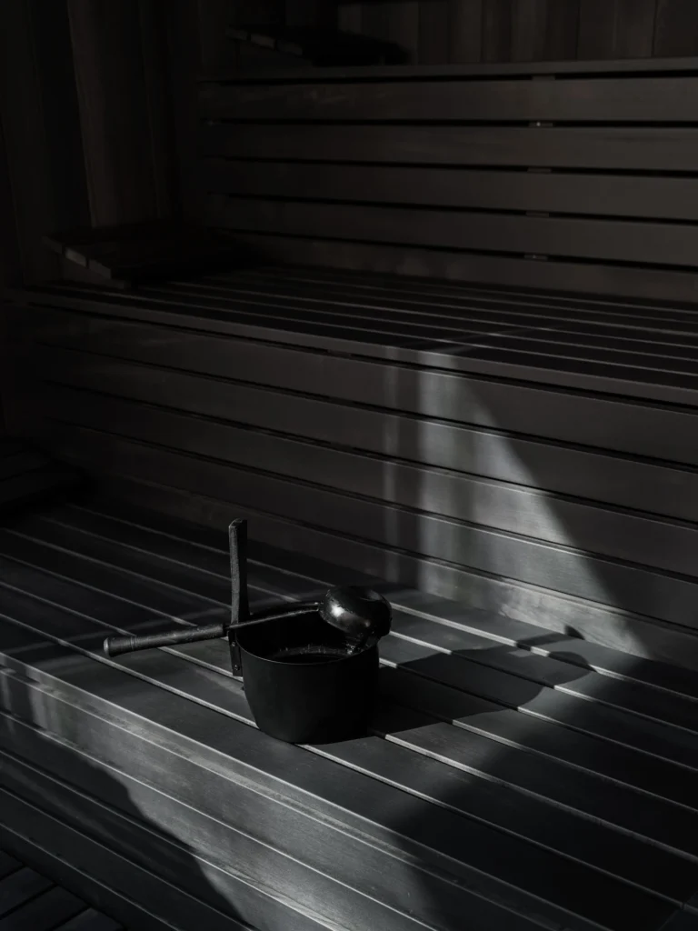 A guest reclines in a deep stone bathtub filled with steaming Alpine herb-infused water in the Sonnwies spa, a panoramic window framing the mountain forest outside.