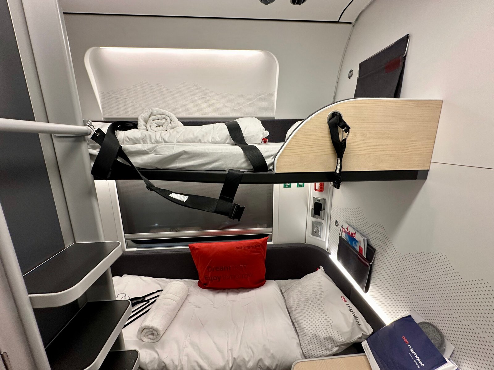 Interior of a new-generation OBB Nightjet sleeping cabin with built-in beds, reading lamps and a window, made up for the night.
