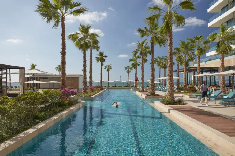 Aerial view of the multiple outdoor swimming pools and sun loungers at Mandarin Oriental Jumeira, Dubai, with the beach and Arabian Gulf beyond