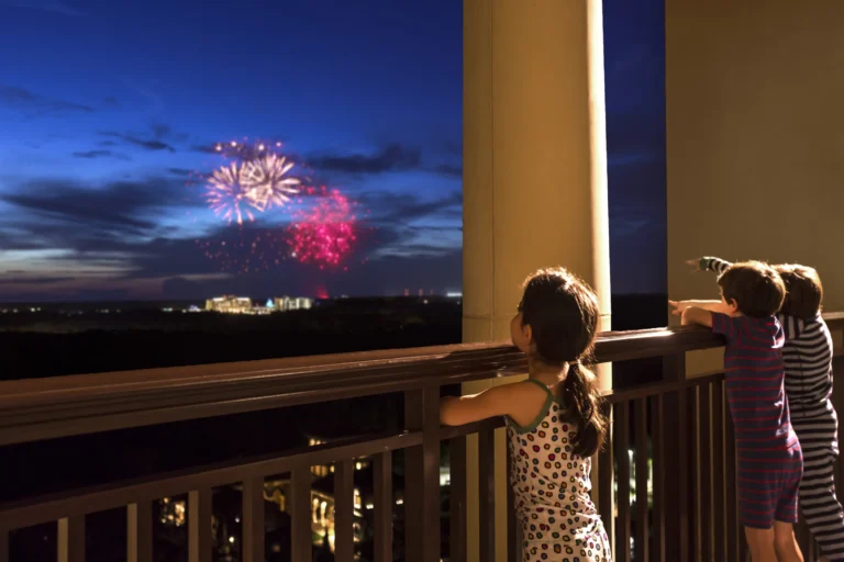 Two children watching Disney fireworks light up the night sky from a resort balcony at Four Seasons Resort Orlando