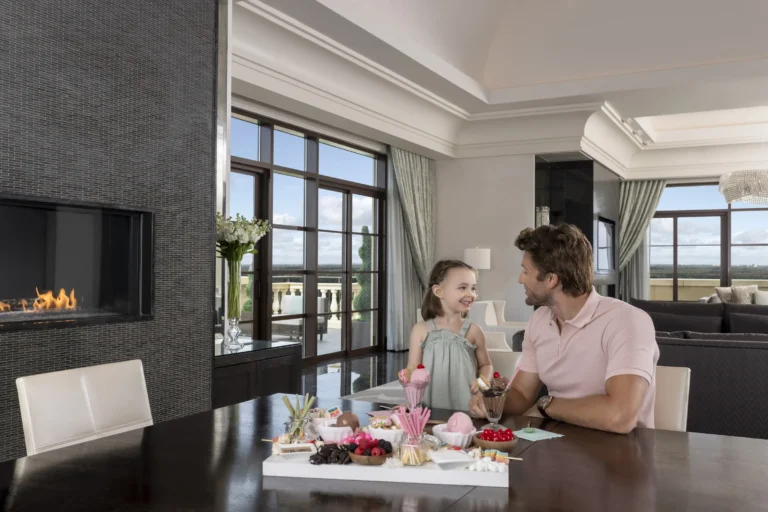 A father and two children enjoying afternoon treats at a dark-wood table in a suite at Four Seasons Resort Orlando