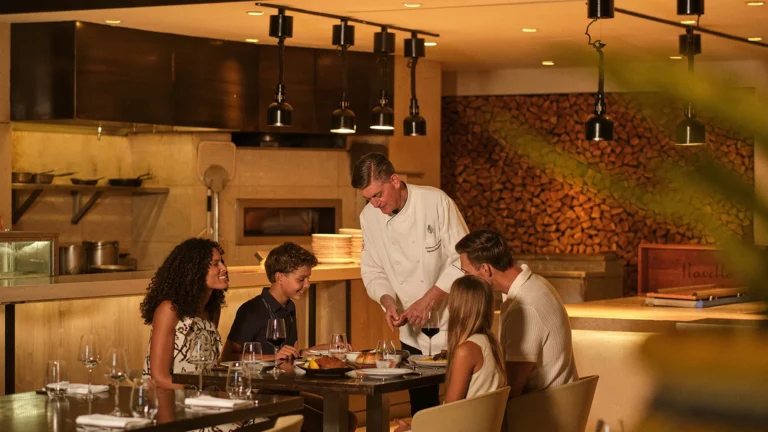 A family of four seated at the open exhibition kitchen counter watching a chef prepare their meal at Four Seasons Resort Orlando