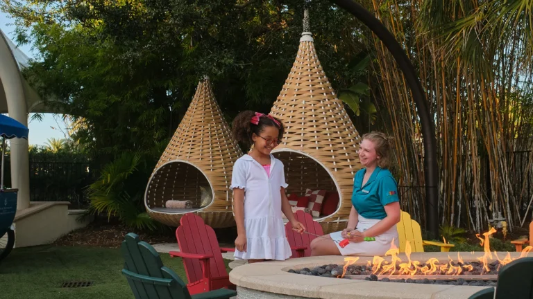 Children in hanging cocoon chairs at an outdoor kids' activity nook, with a staff member preparing an activity, at Four Seasons Resort Orlando