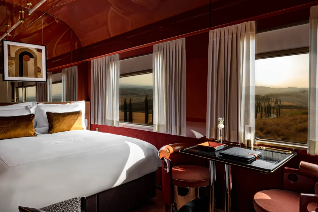 A suite aboard the Orient Express La Dolce Vita, its deep red lacquer interior looking out over golden-hour Tuscan hills and cypress trees