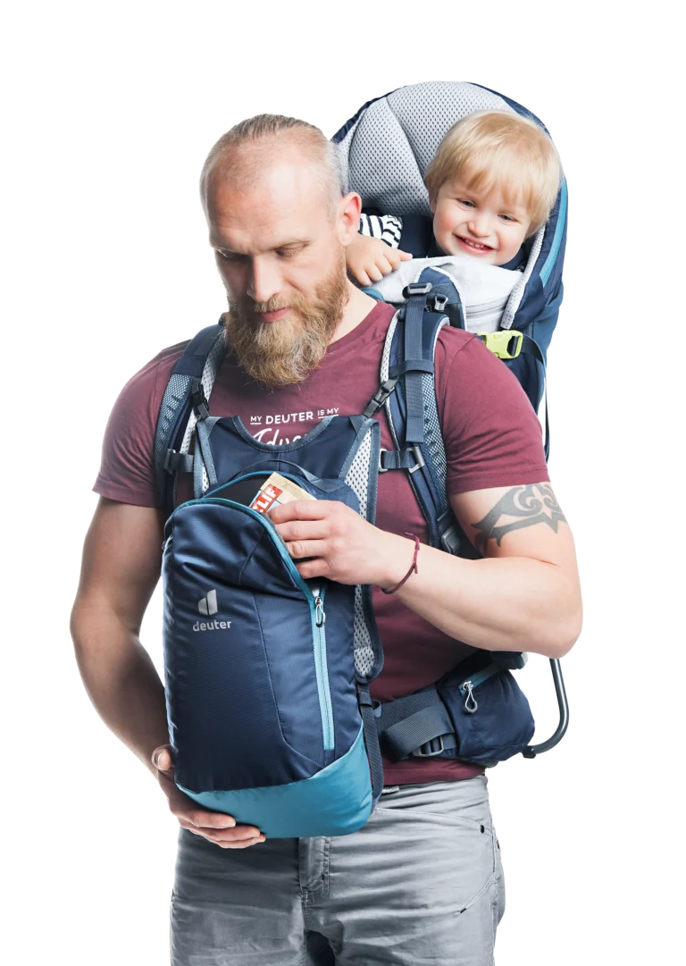 Father wearing the Deuter Kid Comfort Pro with a smiling toddler seated in the carrier, holding the detachable 10-litre daypack at his chest