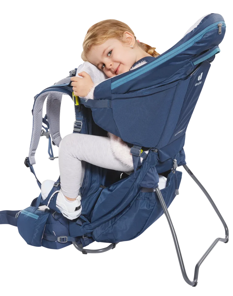 Young child seated and resting comfortably in the Deuter Kid Comfort Pro, which stands free on its kickstand with the side panel and harness visible