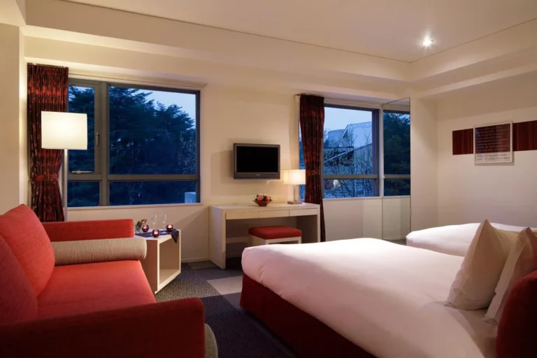 Twin guestroom with red sofa and forest-view windows at dusk at RISONARE Yatsugatake