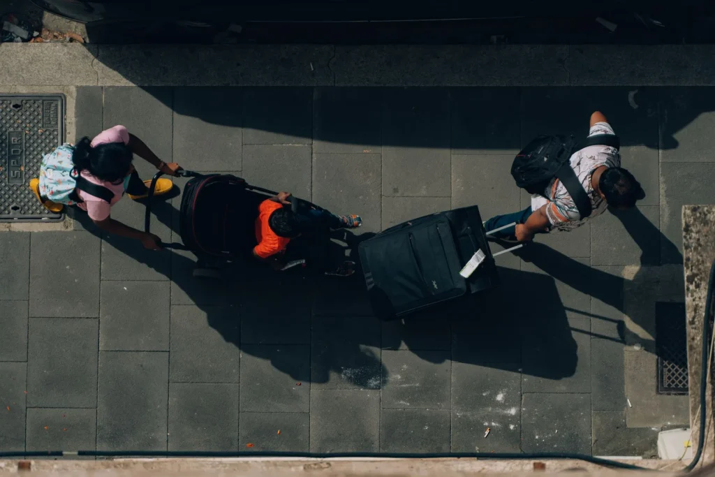 Overhead view of family travellers with luggage and a stroller navigating a cobblestone street in Rome, Italy