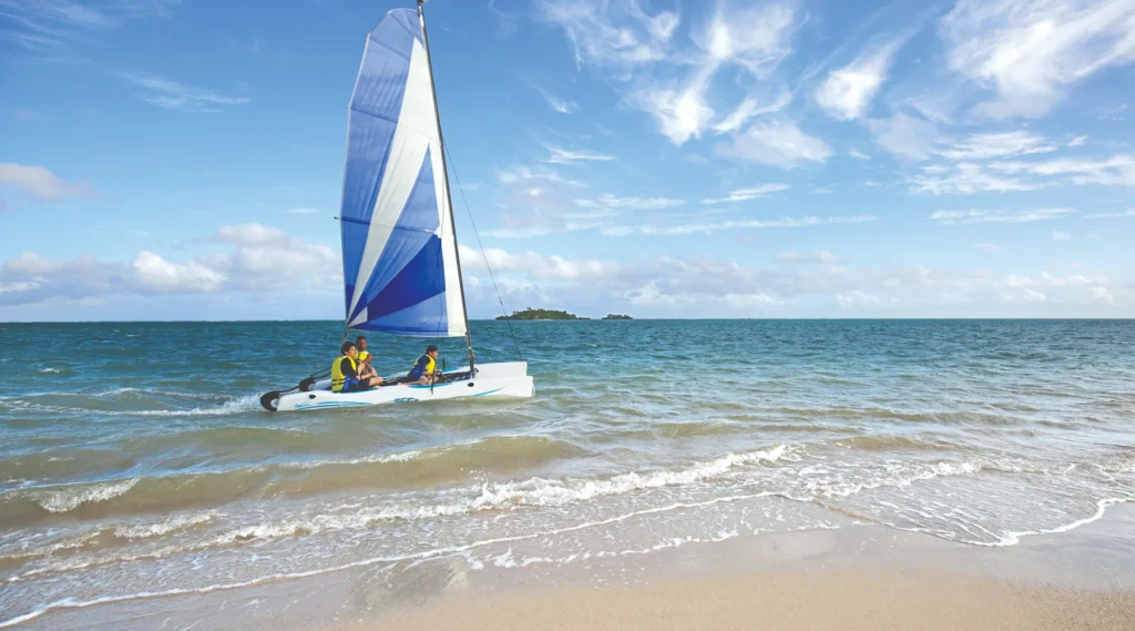 Teenagers sailing a Hobie Cat catamaran on the beach at Jean-Michel Cousteau Resort Fiji, wearing life vests in tropical ocean sunshine
