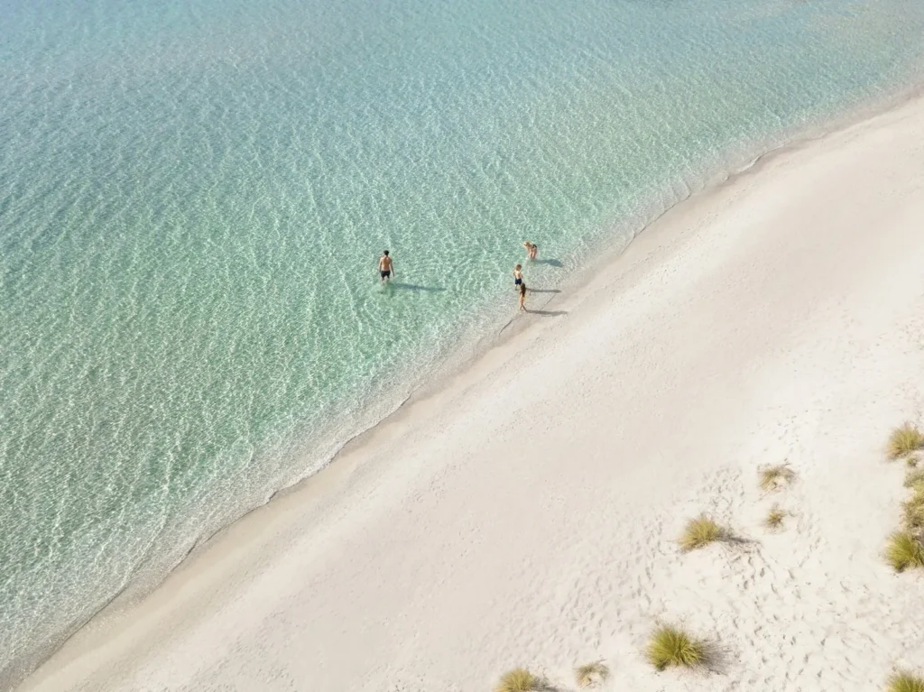 A family relaxing on the calm sandy Bousoulas beach at Sani Resort, Halkidiki, in soft late-summer light