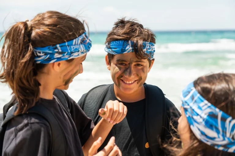 Teenagers in camouflage face paint on the beach during a Bear Grylls Survival Academy session