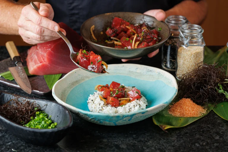 Chef spoons ahi tuna poke over rice in a blue ceramic bowl at Mina's Fish House, Four Seasons Oahu