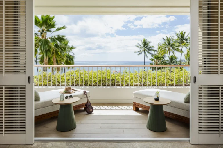 Private lanai of an oceanfront room at Four Seasons Oahu with ukulele, straw hat and views of the Pacific through the palms