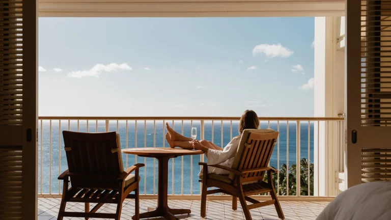 Guest in white bathrobe relaxes on a private oceanfront balcony looking out at the open Pacific Ocean
