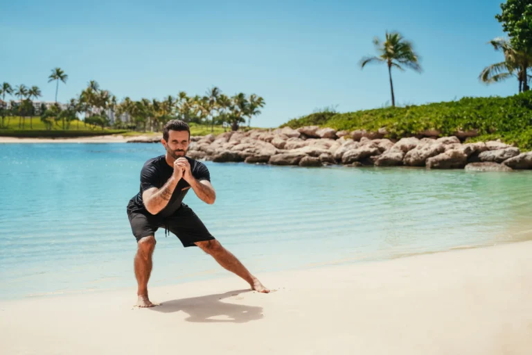 Personal trainer does a beach workout on Ko Olina sand with the resort lagoon and rocky breakwater behind