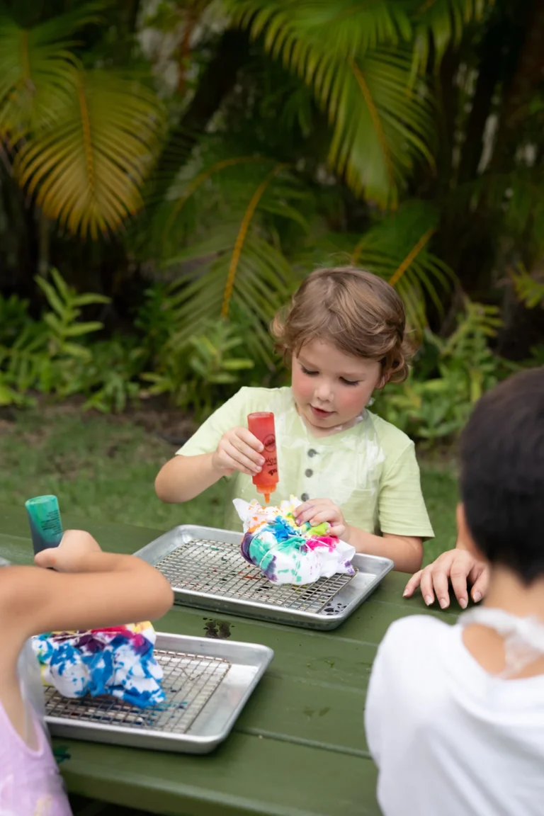 A young child decorating a craft tray outdoors at Camp Kohola, Four Seasons Resort Oahu