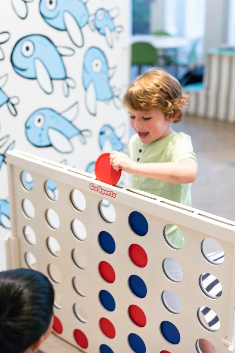 A toddler playing giant Connect Four in the Camp Kohola games area