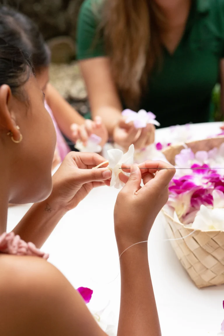 Children stringing plumeria blossoms into lei with a Camp Kohola counsellor at Four Seasons Resort Oahu