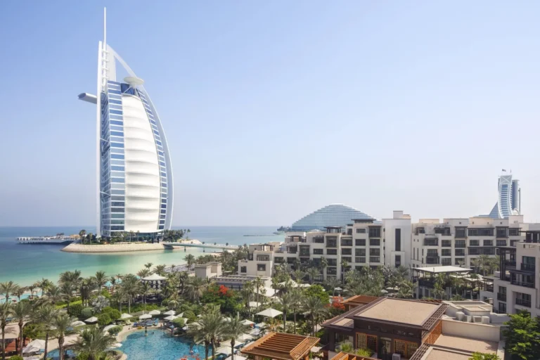 Aerial view of Jumeirah Al Naseem's tropical gardens, free-form pools and private beach with the sail-shaped Burj Al Arab rising immediately behind the hotel
