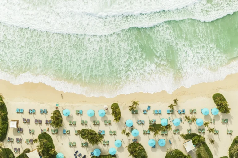 Drone shot looking straight down onto Jumeirah Al Naseem's private white-sand beach — rows of teal parasols and sun loungers line the sand as turquoise Arabian Gulf surf breaks at the edge