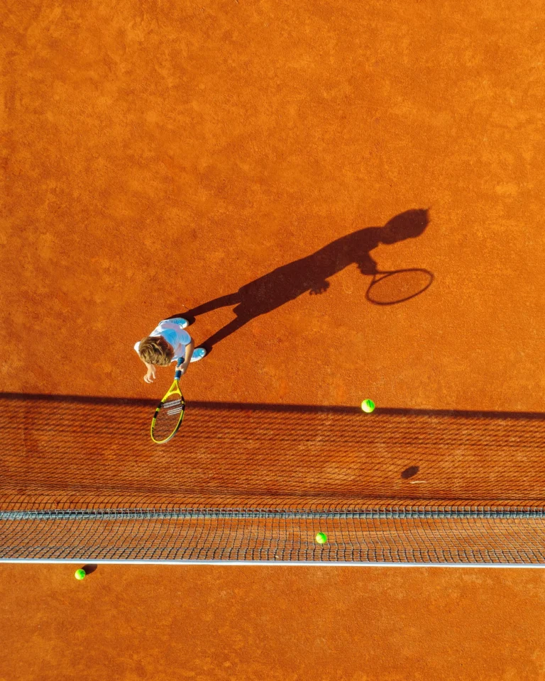 Junior player serving on the clay courts of the Rafa Nadal Tennis Centre at Sani Resort
