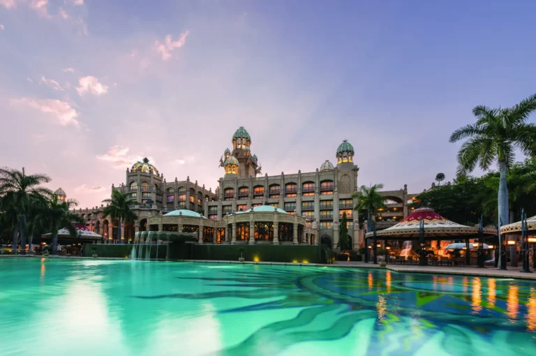 The Palace of the Lost City illuminated at dusk beside the mosaic-tiled Bridge of Time pool