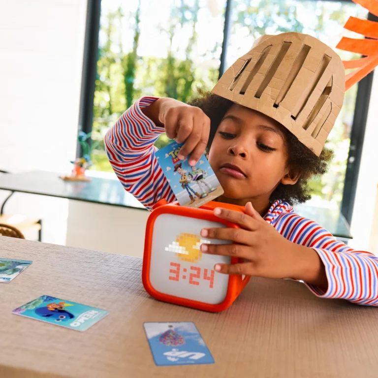 Child in striped top and cardboard knight helmet inserting a Toy Story audio card into the Yoto Player on a table, Disney story cards scattered nearby