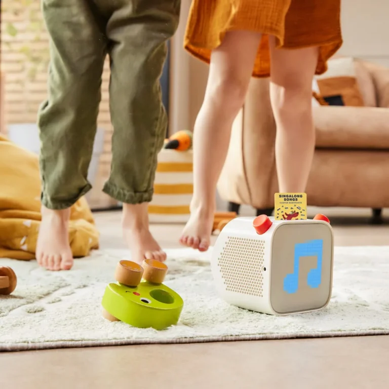 Yoto Player on living room rug playing Singalong Songs with two young children standing and playing nearby, wooden toys scattered on the floor
