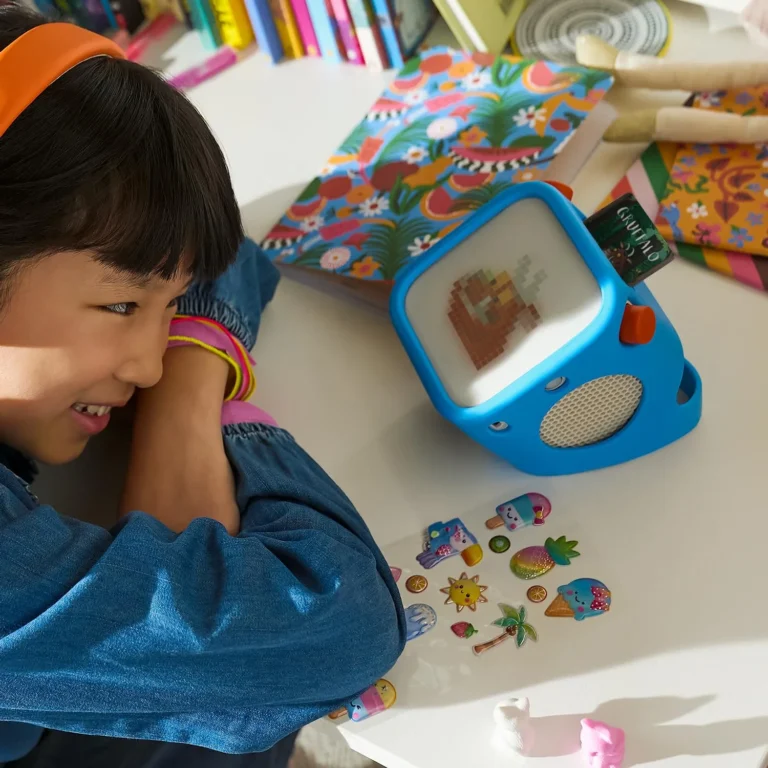 Young girl smiling and listening to the Yoto Player in blue, The Gruffalo card inserted, colourful stickers and art supplies on the desk around her