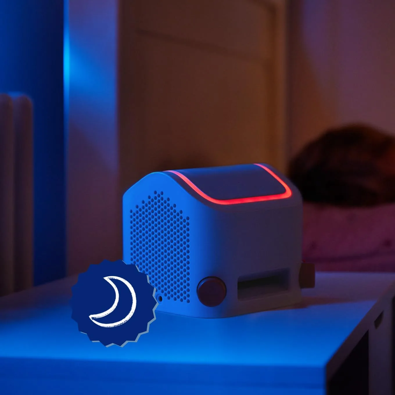 Yoto Player 3rd Generation with amber night light glowing on a wooden hotel bedside table in low evening light