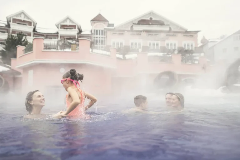 Mothers and children in an outdoor heated pool at Cavallino Bianco in winter, steam rising